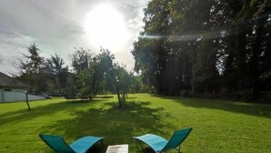 Ein Sitzbereich im Freien mit zwei blauen Stühlen und einem Tisch, umgeben von Gras und Bäumen.