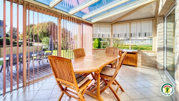 Una veranda con un'ampia volta in vetro, arredi in legno e vista sul giardino.