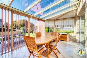 Une véranda avec une grande verrière, des meubles en bois et une vue sur le jardin.