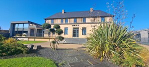 Un bĂątiment moderne, sur lequel on peut lire lâinscription « MAIRIE », et un jardin bien entretenu oĂč poussent diffĂ©rentes espĂšces de plantes.