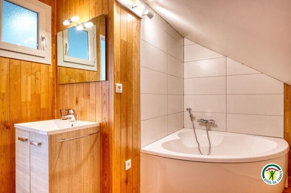 Une salle de bain avec des lambris en bois, un lavabo blanc, un miroir et une baignoire.