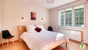 Una camera da letto con un letto in legno, una sedia nera, una finestra vista verde e una lampada a sospensione.