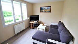 A living room with a TV, a sofa, a small table, and a painting on the wall. - Gîtes de France® - Between Sea and Earth (BAILLY EN RIVIERE)