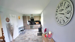 A modern kitchen with a dining area, a large clock, and a vase with flowers. - G îtes de France® - Between Sea and Earth (BAILLY EN RIVIERE)