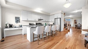 A modern kitchen with white cabinets, a central island with bar stools, and a stainless steel refrigerator.