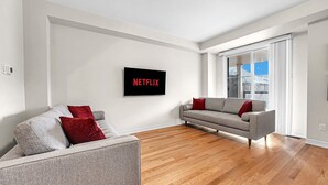 A modern living room with two sofas, a flat-screen TV, and a large window with a view of buildings.