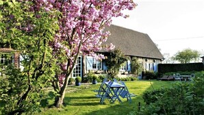A house with a tiled roof, a lawn, and a garden with a tree bearing pink flowers. - Gîtes de France® - La Roselière (SAINTE COLOMBE)