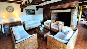 A cozy lounge area with wicker furniture, a fireplace, and a clock on the wall. - Gîtes de France® - La Roselière (SAINTE COLOMBE)