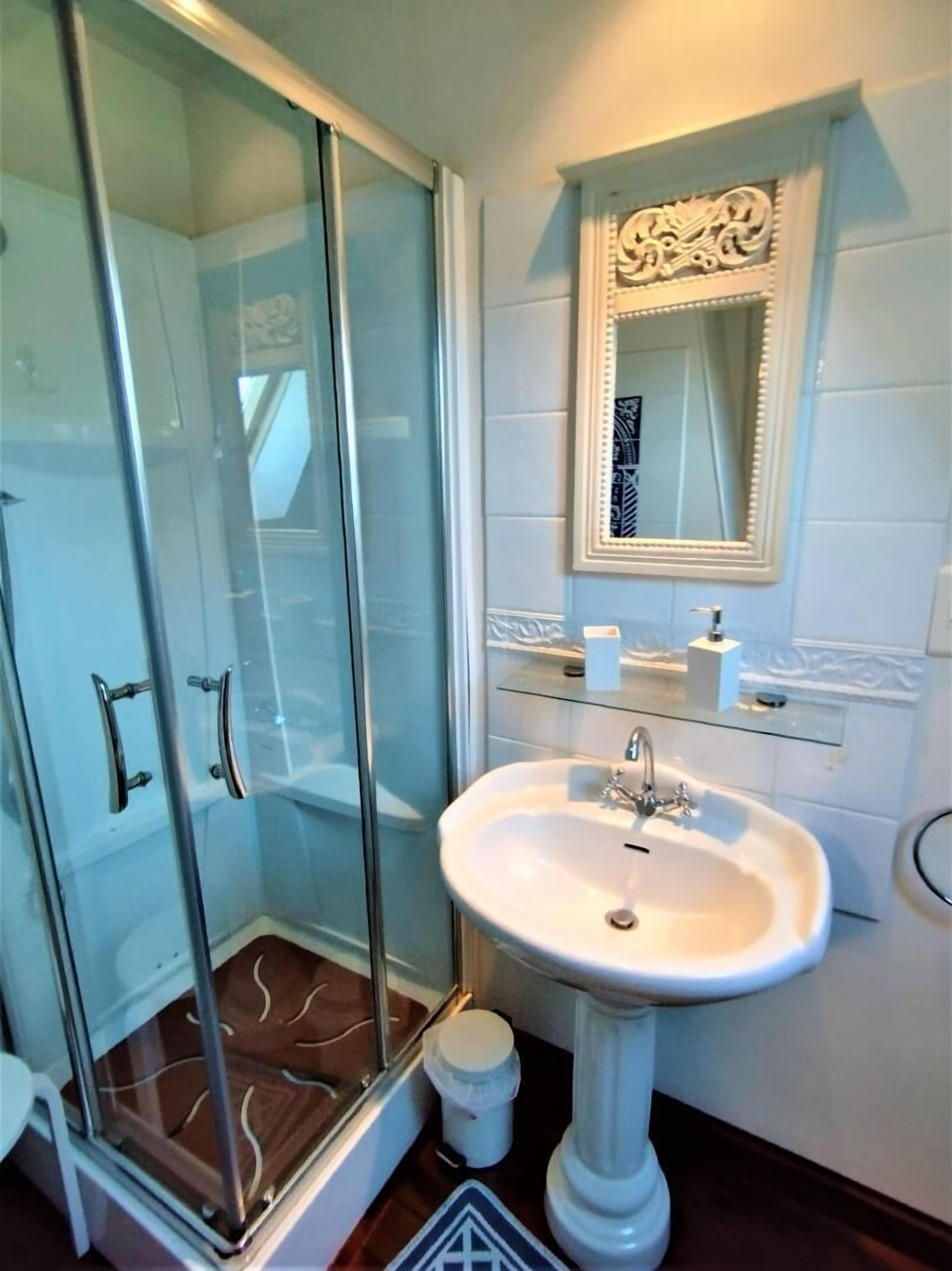 A bathroom with a glass shower enclosure, a pedestal sink, and a mirror with decorative molding.