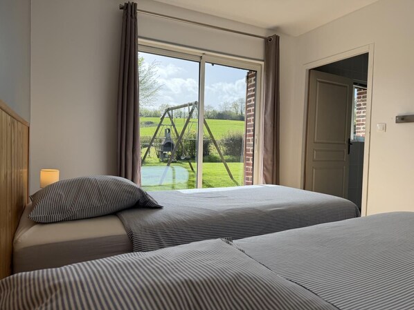A bedroom with a large window, a bed with striped bedding, and a view of a swing set and greenery outside.