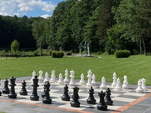 A chessboard set up outdoors with a park and statue in the background. - Gîtes de France® - Giteopré (BEAUBEC LA ROSIERE)