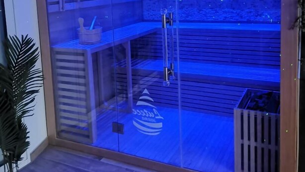 Eine Sauna mit Glasfront, Holzinnenraum und einem Sternenhimmel-Lichtsystem.