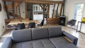 Ein modernes Wohnzimmer mit Ecksofa, einem Essbereich unter einer Holzbalkendecke und einer Küche im Hintergrund.