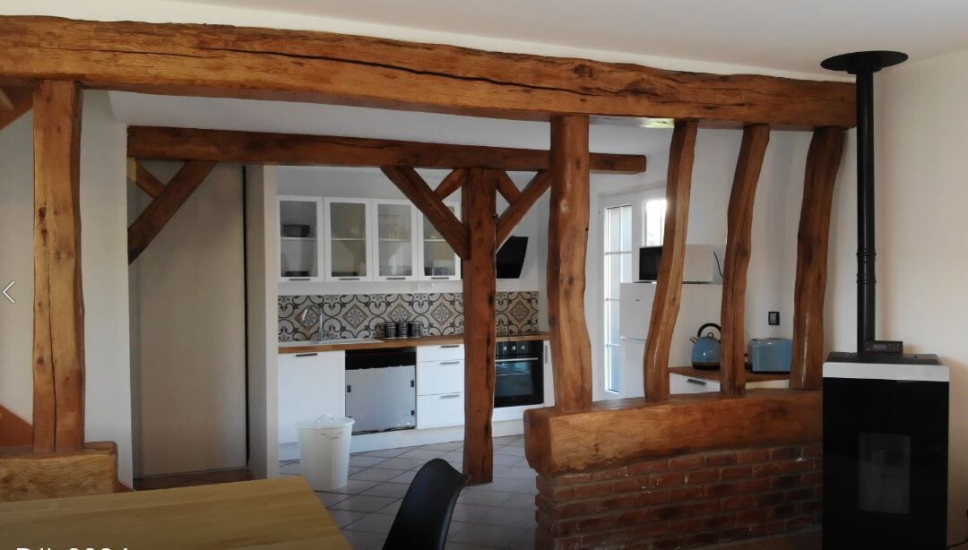 Une cuisine rustique avec des poutres en bois apparentes, des meubles blancs et un poêle noir.