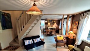 Amplia sala de estar con sofá negro, mesa de centro de madera y mesa de comedor con sillas. Una escalera conduce a un nivel superior.