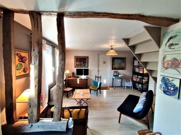 A cozy living room with a wooden beam, a dining area, and a staircase leading to another level.