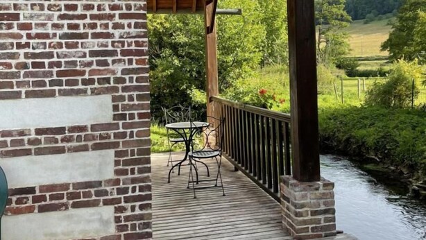 Una terraza de madera con un muro de ladrillo, una barandilla metálica y una mesa con sillas.