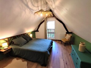 Cozy attic retreat with a bed, nightstand, chair, and dresser, offering a serene view of the surrounding greenery.