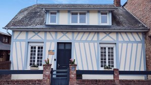 Une maison traditionnelle à colombages, avec une porte bleu foncé, des fenêtres à cadre blanc et une cheminée.