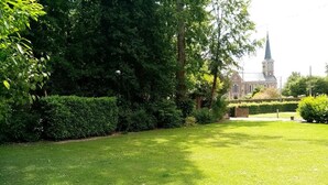 A well-maintained lawn with a large tree and a building with a steeple in the background. - Gîtes de France® - Le Petit Gîte (ERMENOUVILLE)