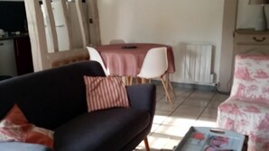 A living room with a dark sofa, a coffee table with a box of items, a dining table with chairs, and a wall with a quote. - Gîtes de France® - Le Petit Gîte (ERMENOUVILLE)