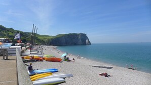 Ein Strand mit an der linken Seite angeordneten Kajaks, einem felsigen Felsen im Hintergrund und einem klaren, blauen Himmel.