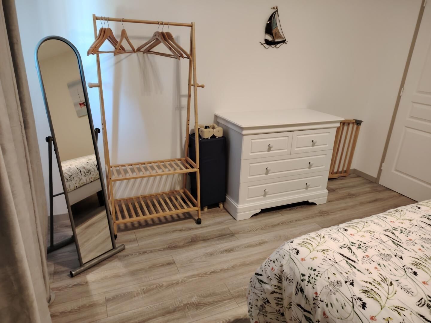 Une chambre à coucher avec une armoire en bois, un miroir, une commode et un lit avec une literie à motifs floraux.