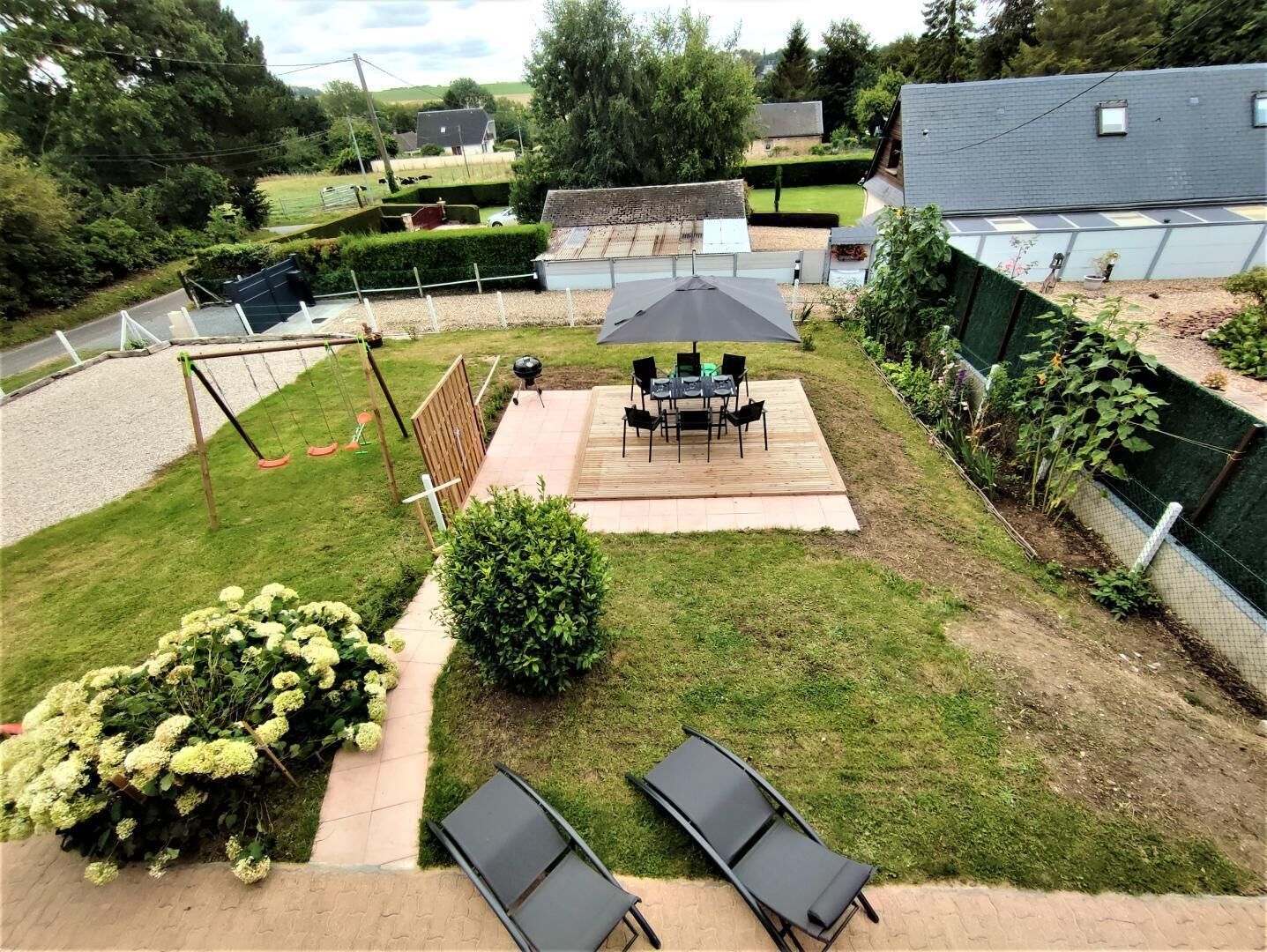 A backyard with a patio, a swing set, and a garden with hydrangeas.