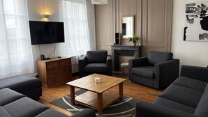 A modern living room with a flat-screen TV, dark sofas, a wooden coffee table, and a fireplace. - Gîtes de France® - Gîte du Loup Vert (JUMIEGES)