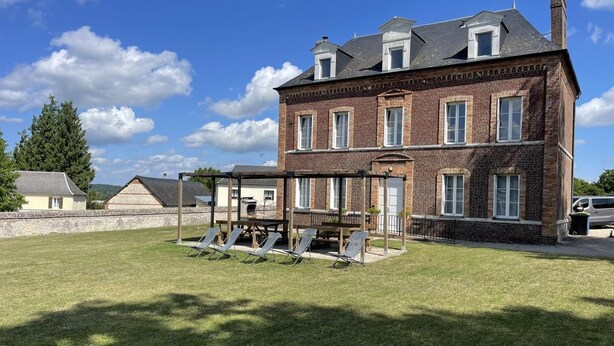 A large brick building with a well-maintained lawn and outdoor seating area. - Gîtes de France® - Gîte du Loup Vert (JUMIEGES)