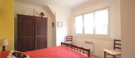 Une chambre à coucher avec un lit, une armoire en bois, une chaise, une petite table et une fenêtre avec des rideaux.
