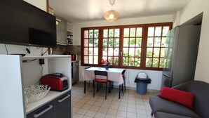 A compact kitchen with a dining table, chairs, a sofa, and a trash bin.