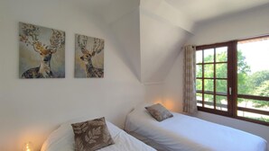 A bedroom with two beds, a window with curtains, and two wall-mounted paintings.