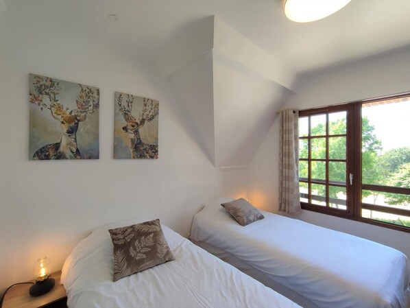 A bedroom with two beds, a window with curtains, and two wall-mounted paintings.