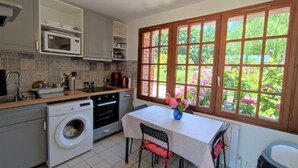 A kitchen with a washing machine, a dining table with chairs, and a window with a view of greenery.