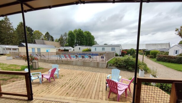 Una terraza de madera con sillas y vistas a un camping con cabañas y una piscina.