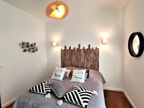 Een slaapkamer met een houten hoofdeinde, twee wandlampen, een hanglamp en een spiegel aan de muur.