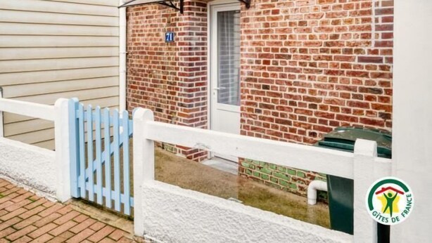 A brick building with a white door and window, a blue sign, and a white fence. - Gîtes de France® - La Mouette (LE TREPORT)
