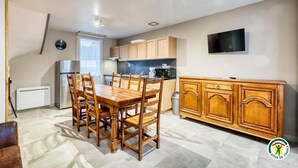 A compact kitchen with wooden cabinets, a dining table with chairs, a built-in oven, and a TV mounted on the wall. - Gîtes de France® - La Mouette (LE TREPORT)