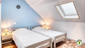A bedroom with two beds, a skylight, a clock, and a nightstand with a lamp. - Gîtes de France® - La Mouette (LE TREPORT)