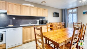 A modern kitchen with wooden cabinets, a black countertop, and a dining area with a wooden table and chairs. - Gîtes de France® - La Mouette (LE TREPORT)