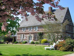 Une maison traditionnelle à colombages, dotée d’une pelouse bien entretenue et d’un fauteuil de jardin blanc.