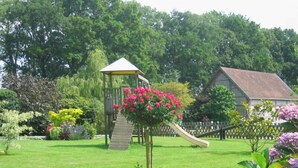 Un giardino con una struttura di gioco in legno, uno scivolo e diverse piante fiorite.