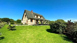 A large, two-story house with a sloped roof, a covered porch, and a well-maintained lawn. - Gîtes de France® - La Demeure des Vents (LE TILLEUL)