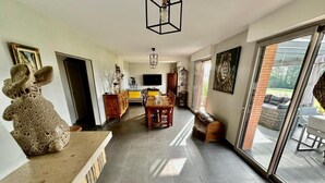 A spacious living area with a long dining table, a large window, and a sculpture on the left. - Gîtes de France® - La Demeure des Vents (LE TILLEUL)