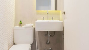 Une salle de bain avec des toilettes blanches, un lavabo blanc avec un miroir au-dessus, et une petite plante en pot posée sur le réservoir des toilettes.