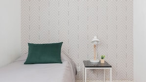 Un lit bien fait, avec un oreiller vert et une lampe blanche posée sur une petite table à côté.