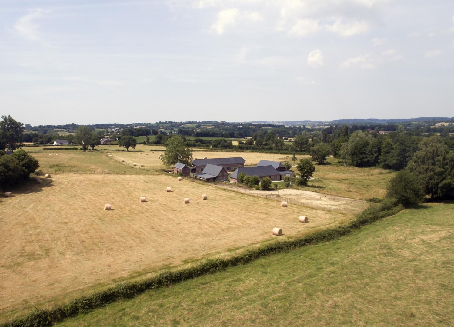 A rural landscape with a farmstead, hay bales, and a clear sky.