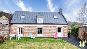 A two-story brick house with a sloped roof, a small attached garage, and a well-maintained lawn with outdoor seating.