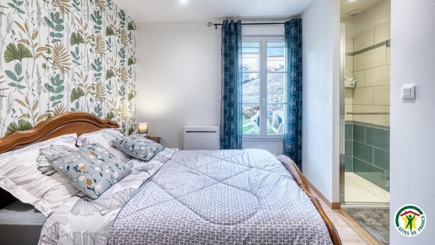 A bedroom with a bed, a window with curtains, a radiator, and a shower area.